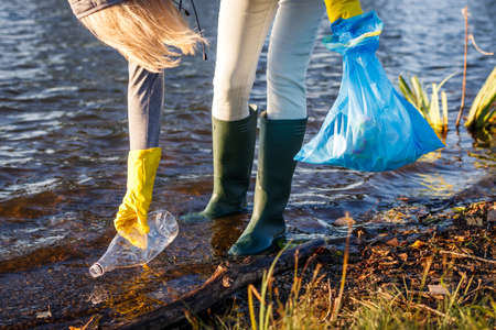 Volunteer picking up plastic bottle from polluted lake or river. Environmental damage. Water pollution with plastic garbageの写真素材