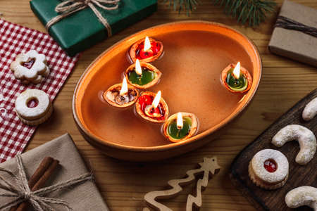 Burning candles made from nutshell floating on water. Christmas tradition. Decoration, christmas sweets and gift on tableの写真素材