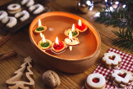 Christmas tradition. Candles made from nut shell floating on water. Decoration and christmas sweets on tableの写真素材