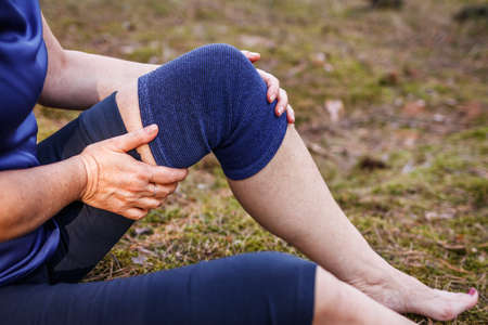 Hiker putting elastic orthopedic bandage during hiking. Woman feeling joint and knee pain after injury. First aid of torn ligament or knee sprain fixation outdoorsの写真素材
