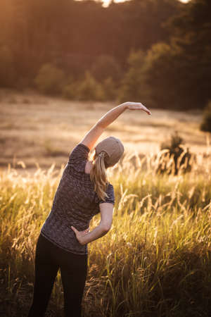 Stretching and warm up exercise before jogging in nature. Woman is doing cardiovascular exercise outdoors during sunset. Fitness active lifestyleの写真素材