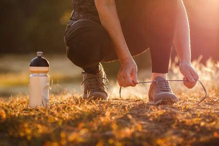 Woman tying shoelace of running shoe. Getting ready for jogging outdoors during sunset. Fitness, running and active lifestyleの写真素材