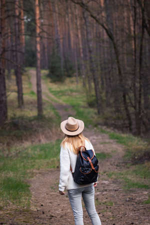 Woman with cowboy hat and backpack hiking on footpath in forest. Exploring new journey in natureの写真素材