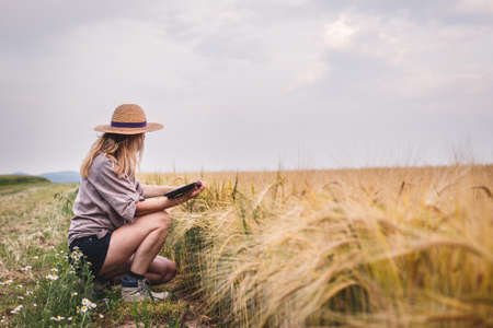 Farmer working in barley field and examining quality of produce before harvest. Woman using digital...