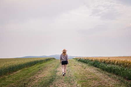 Farmer inspecting and examining agricultural field with cereal plant. Woman with straw hat and digital tablet walking in her organic farmの写真素材