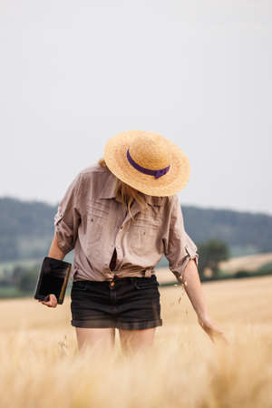 Farmer inspecting and examining agricultural field before harvest. Woman with straw hat and digital...