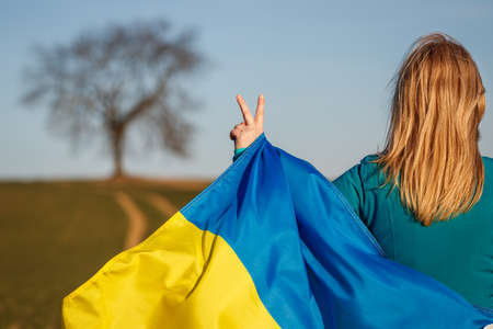 Woman with ukrainian flag is hand gesturing peace or victory symbol.の写真素材