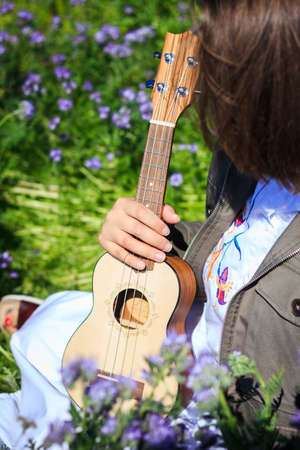 Ukulele music instrument in female hand. Woman sitting in flowers at springの写真素材
