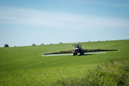 Tractor spraying insecticide at field. Agricultural activity at springtime. Cultivated land in countrysideの写真素材