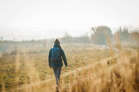 Woman with backpack hiking on footpath at cold morning. Fall exploration outdoorsの写真素材