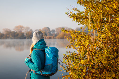 Woman tourist with backpack hiking at lake in autumn. Exploration nature during fall seasonの写真素材
