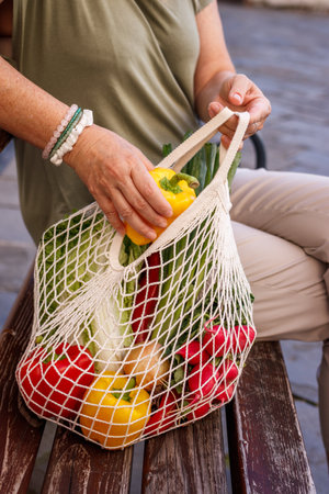 Woman with mesh bag sitting on bench in city. Plastic free shopping and sustainable lifestyle conceptの写真素材