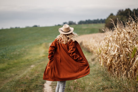 Happy woman with cowboy hat and red coat running at corn field. Fall season in the countryside. Autumn fashion collectionの写真素材