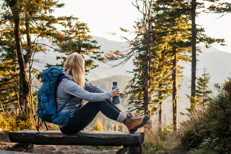 Woman with backpack and flask resting on bench in forest. Relaxation during hiking in the mountainの写真素材