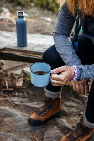 Woman hiker taking a break with hot drink during mountain trekking. Refreshment with a cup of teaの写真素材