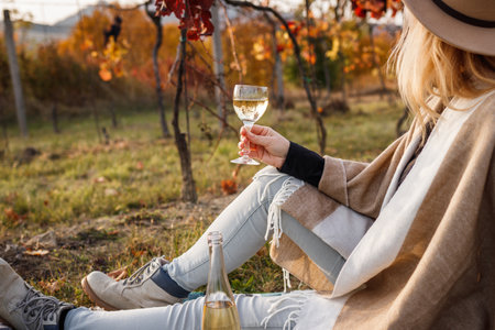 Woman sitting in vineyard and drinking white wine. Relaxation in fall winery after grape harvestingの写真素材