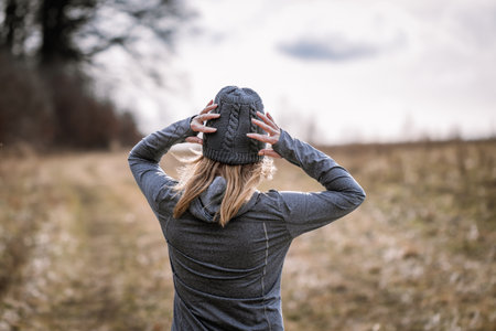 Female athlete puts on hat in cold weather before running outdoors. Woman jogging and exercising in autumn natureの写真素材