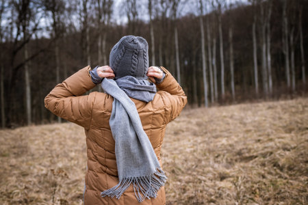Wind and cold weather in the fall season. Woman wearing coat, scarf and knit hat outdoorsの写真素材