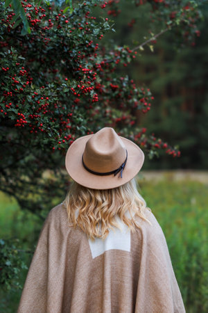 Woman with hat and poncho standing under hawthorn tree in autumn nature. Hippie fashion styleの写真素材