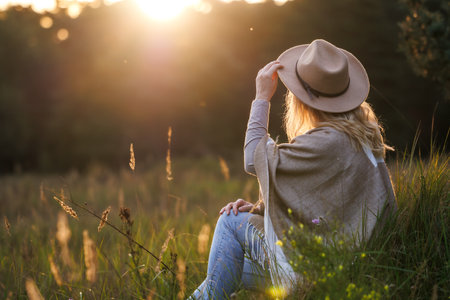 Happy woman with hat and poncho relaxing outdoors during sunset. Mental well-being and resting in natureの写真素材