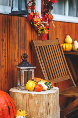 Autumn halloween decoration with lantern and pumpkin on tree trunk next wooden cabin. Garden furniture at patioの写真素材