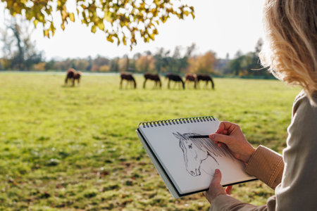 Pencil drawing. Woman artist sketching horse outdoors. Illustrator making sketchの写真素材
