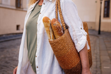 Woman with baguette bread in straw bag. Sustainable lifestyle and reusable shopping bagの写真素材