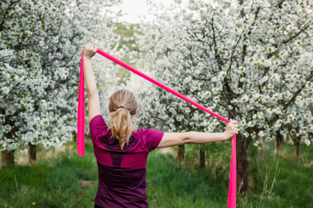 Woman exercising with elastic resistance band in spring nature. Fitness stretching exercise. Sports activities outdoorsの写真素材