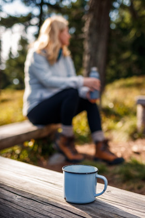 Travel mug on wooden bench. Relaxation during hiking outdoors. Woman camping in forestの写真素材