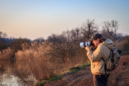 Landscape photographer with camera and telephoto lens photographing wildlife in nature during sunsetの写真素材