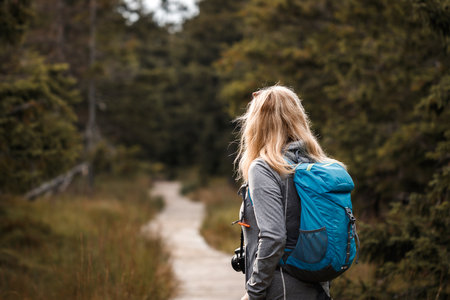 Woman tourist with backpack and camera hiking on wooden path in mountains forestの写真素材
