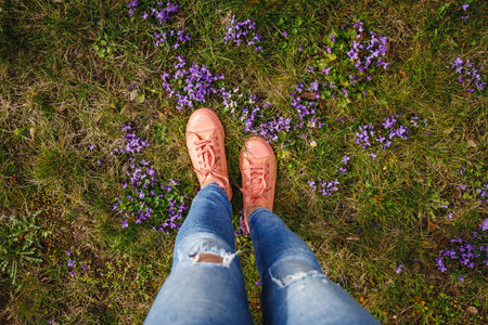 Woman wearing jeans and pink sneakers walking in grass with violet flowers. Spring fashion seasonの写真素材