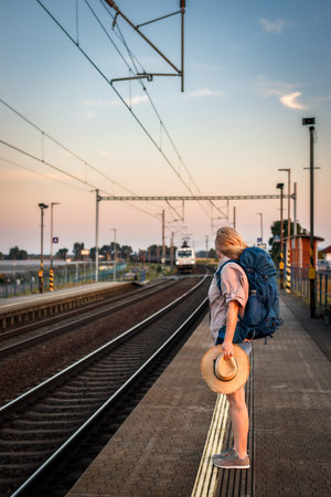 Woman traveler waiting at train station during sunset. Solo tourist is ready for summer journeyの写真素材