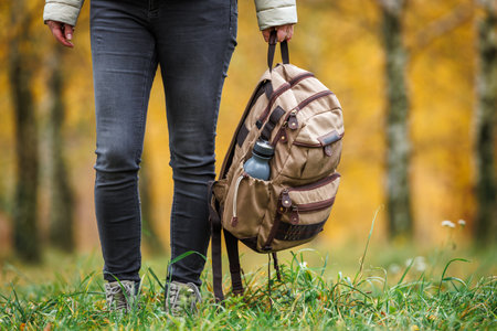 Female hiker holding backpack in hand. Woman trekking in autumn forest. Adventure in natureの写真素材