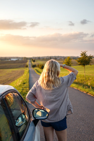 Summer road trip. Woman traveling by car and standing on road during sunsetの写真素材