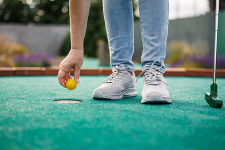 Woman plays mini golf and taking ball out of the hole after successful puttingの写真素材