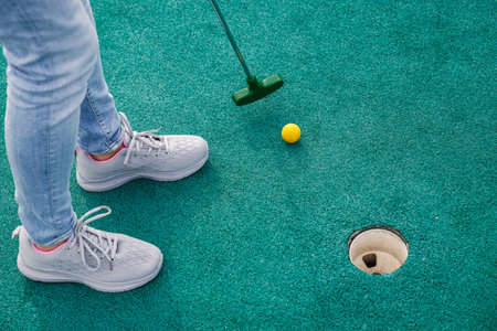 Woman playing miniature golf and trying to put ball into hole. Summer leisure activityの写真素材
