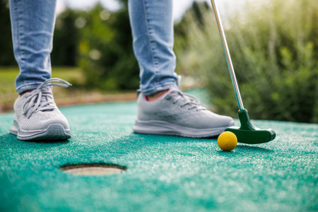 Golfer playing mini golf and trying putting ball into hole. Summer leisure activityの写真素材