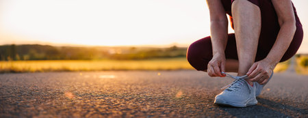 Woman tying shoelaces on her running shoes. Preparation before jogging on the road during sunset. Fitness and sports activitiesの写真素材