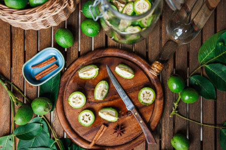 Making homemade walnut liqueur. Unripe nuts, alcohol in bottle and knife on cutting board on tableの写真素材
