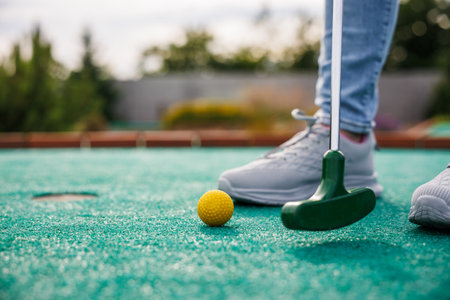 Golfer playing miniature golf and trying putting ball into hole. Leisure activities during summerの写真素材