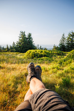 Relaxation in mountain forest during trekking. Crossed male legs with leather hiking bootsの写真素材