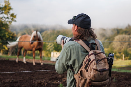 Man photographer with camera and telephoto lens photographing horse at ranch