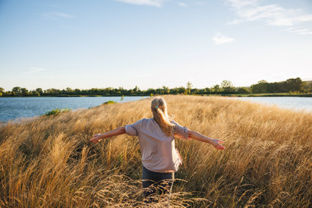 Happy woman with arms outstretched feeling fresh air in hair and enjoying windy weather at lake. Relaxation in natureの写真素材