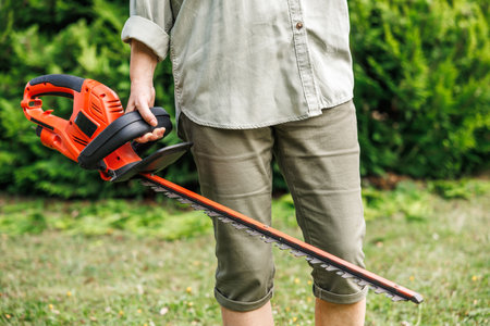 Woman gardener holding electric hedge trimmer. Unrecognizable person is ready for trimming at backyard. Gardening equipmentの写真素材