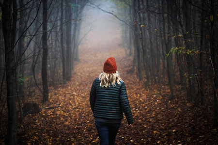 Lonely woman walking on footpath in dark foggy mystery forest. Spooky atmospheric mood in autumn woodlandの写真素材