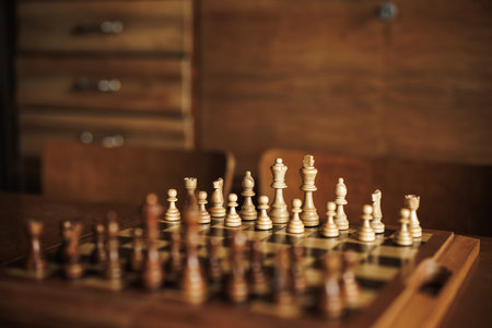 Wooden chess board with set of chess pieces on table. Retro furniture in living room. Selective...