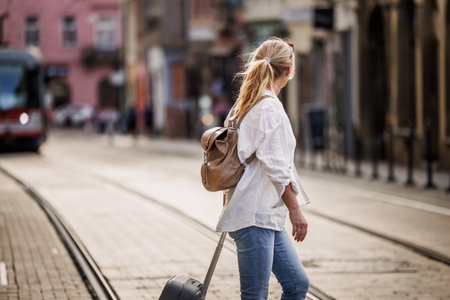 Woman tourist with suitcase walks across street with tram tracks in city. Travel and vacation lifestyleの写真素材