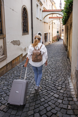 Woman traveler with suitcase and backpack walking on street. Travel and vacation in European city Olomouc, Czech Republicの写真素材