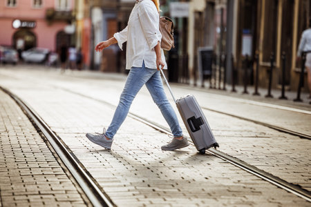 Woman tourist with suitcase walks across street with tram tracks in city. Travel and vacation lifestyleの写真素材